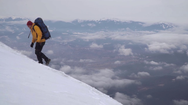 一个旅行者在爬白雪覆盖的山坡视频素材