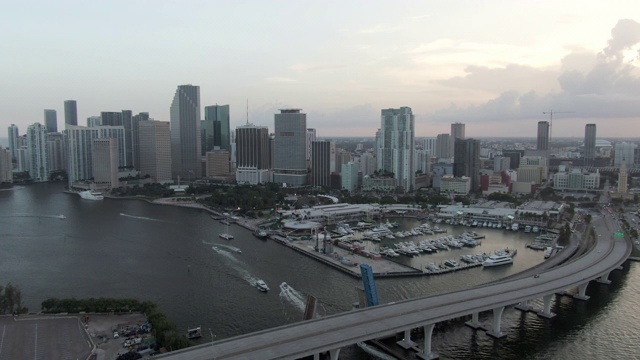 航拍港口和建筑物在天空下的海上船只，日落时无人机在城市的桥上向后飞行，航拍海上船只视频素材