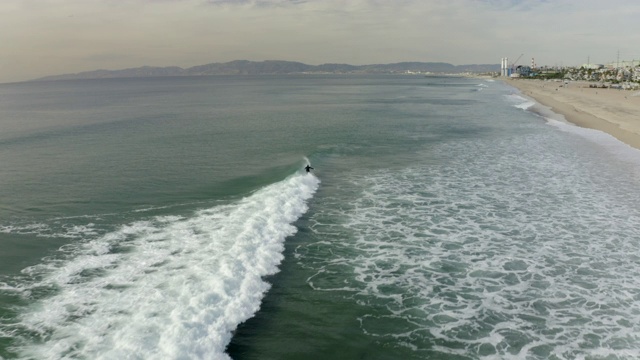 航拍的人在海浪上冲浪对天空，无人机在城市-曼哈顿海滩海岸线向前飞行，加利福尼亚视频素材