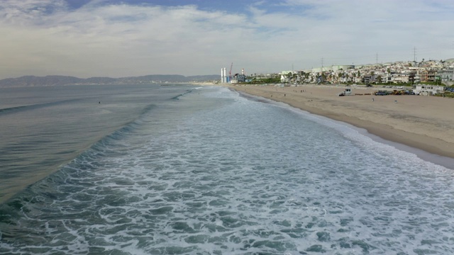 航拍海浪拍打在海滩上的天空，无人机飞向城市的建筑物-曼哈顿海滩，加利福尼亚视频素材