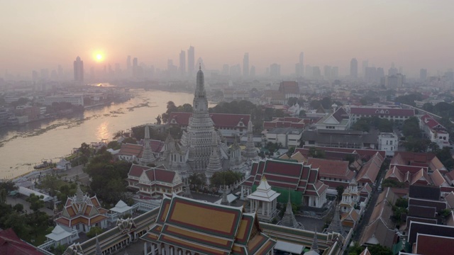 航拍的佛教寺庙在城市的河流在日落，无人机上升在著名的地标对天空-曼谷，泰国视频素材