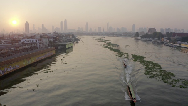 空中封锁拍摄的船只在城市的河流上前进，无人机在日落时分飞过水面-泰国曼谷视频素材