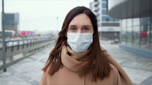 流行的保护。在隔离期间，美丽的白人妇女在空旷的城市街道上戴着医用口罩的肖像。视频素材