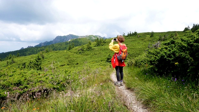 年轻的女孩徒步旅行者与背包与智能手机在山径拍照视频素材