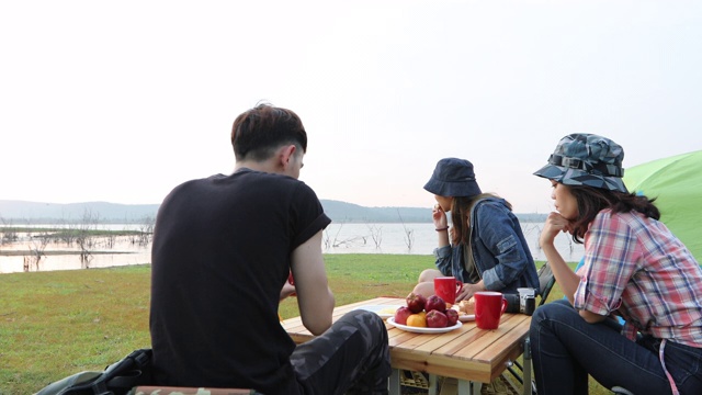 一群亚洲朋友在夏天一起喝酒和弹吉他，在日落时分在湖边露营视频素材