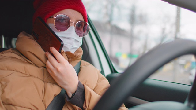 慢镜头:年轻女子戴着医用防护口罩在车里，正在讲手机。呼叫救援服务，冠状病毒大流行概念。视频素材