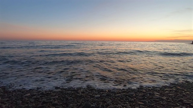 在落日的余晖中，岸上汹涌的波浪美丽的风景。在太阳从地平线升起的背景下，平静的海浪。视频素材