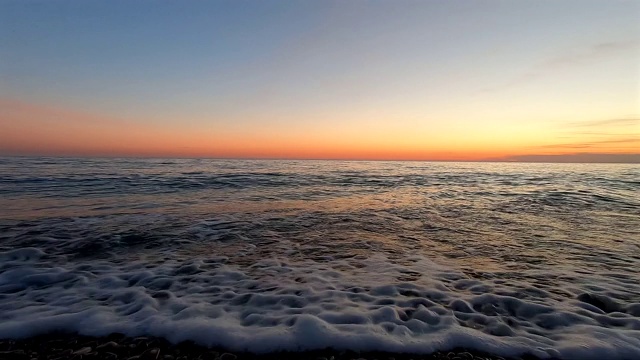 在落日的余晖中，岸上汹涌的波浪美丽的风景。在太阳从地平线升起的背景下，平静的海浪。视频素材