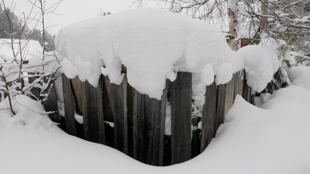 下雪时，俄罗斯一个村庄的旧木栅栏被雪覆盖。4 k视频素材