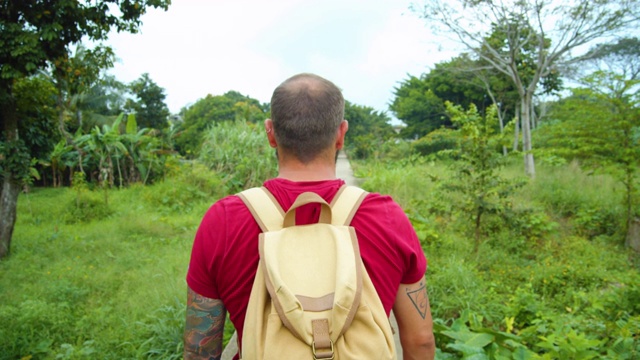 背包徒步旅行者被热带气候景观包围。红色和绿色视频素材