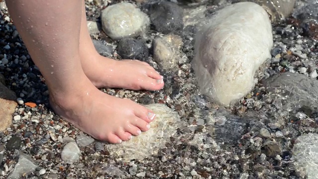 石头沙滩和一双被海浪洗过的女人的脚视频素材