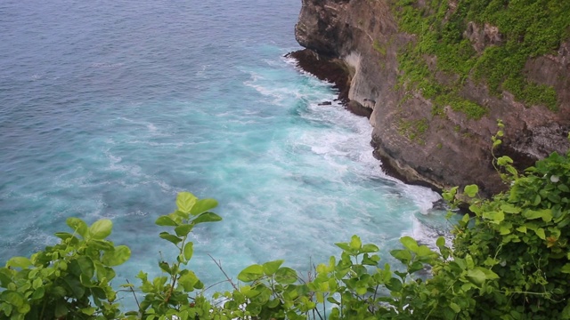 空中静态的黄昏海面，平静的波浪翻滚在岩石海岸。惊人的高悬崖之上的海洋和顶部的乌鲁瓦图寺庙。印尼巴厘岛视频下载