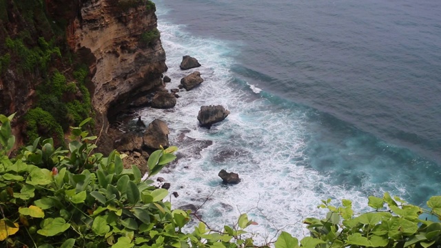 空中静态的黄昏海面，平静的波浪翻滚在岩石海岸。惊人的高悬崖之上的海洋和顶部的乌鲁瓦图寺庙。印尼巴厘岛视频素材