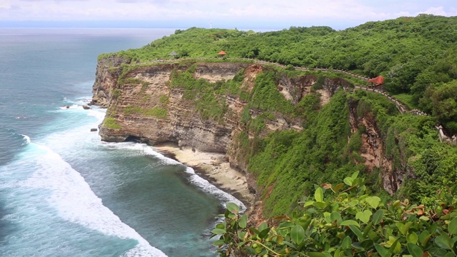 空中静态的黄昏海面，平静的波浪翻滚在岩石海岸。惊人的高悬崖之上的海洋和顶部的乌鲁瓦图寺庙。印尼巴厘岛视频素材