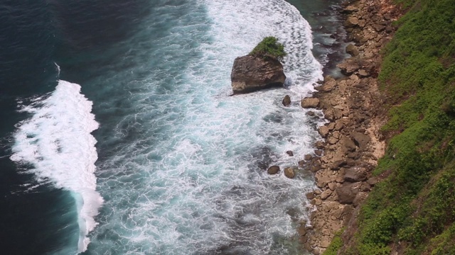 空中静态的黄昏海面，平静的波浪翻滚在岩石海岸。惊人的高悬崖之上的海洋和顶部的乌鲁瓦图寺庙。印尼巴厘岛视频下载