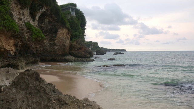 空中静态的黄昏海面，平静的波浪翻滚在岩石海岸。惊人的高悬崖之上的海洋和顶部的乌鲁瓦图寺庙。印尼巴厘岛视频素材