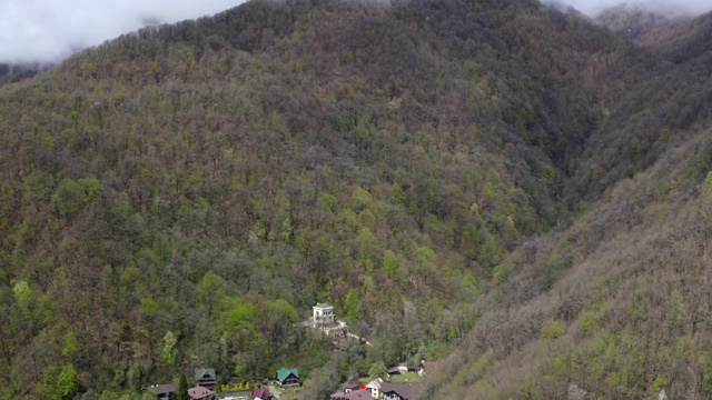 青山峡谷里的房子覆盖着夏天的森林。空中拍摄的高原上覆盖着青翠的森林，山峰上弥漫着薄雾。无人机起飞拍摄山顶雾霾视频素材