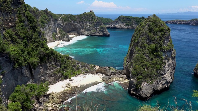 无人机拍摄的热带海滩，海石，绿松石海洋和棕榈树。阿图海滩，努沙佩尼达岛，巴厘岛，印度尼西亚。广受欢迎的旅游景点和旅游目的地视频素材