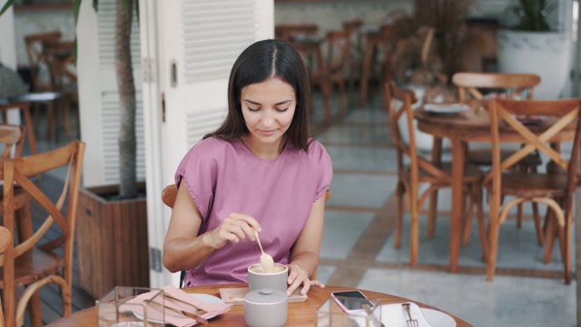 年轻女子在咖啡馆喝咖啡，往饮料里加糖，用勺子搅拌视频素材