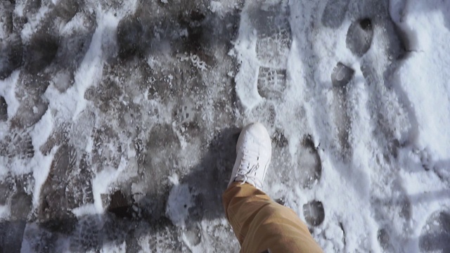 男子在白色运动鞋走在一个潮湿的雪泥泞的道路在春天POV视频视频素材