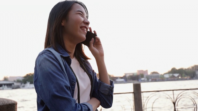 美丽的亚洲女商人与商业伙伴通电话，而站在湄南河在泰国日落。视频素材