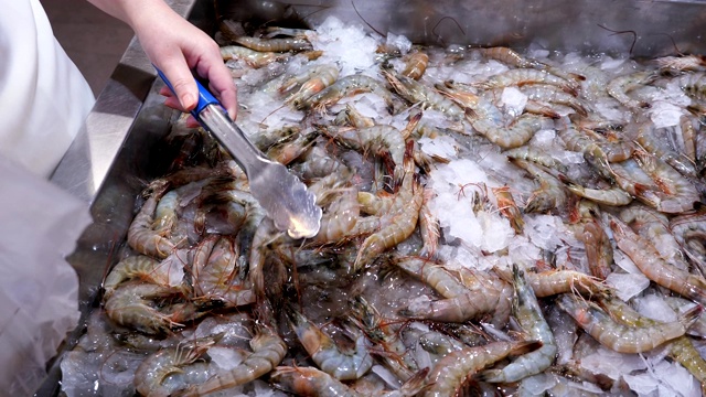 在商店柜台上，一位女士的手将新鲜的生虾在冰水中折叠成一袋视频素材