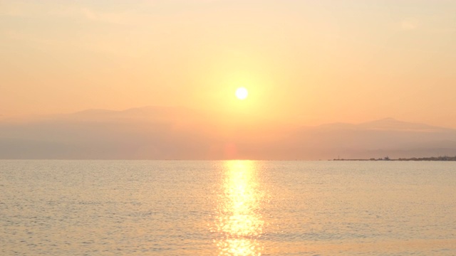 惊人美丽的日出在平静的海面上。黄色的太阳从海和山升起，太阳的路径在水上。阳光和太阳光反射在水面上。金色的光，橙色和金色的蓝天视频素材