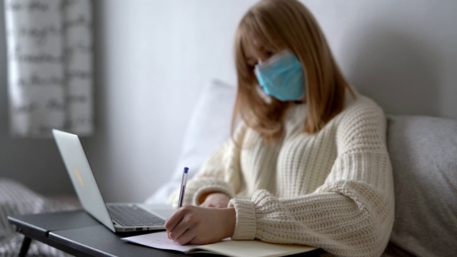 女学生戴着医用口罩在家做学校作业视频素材