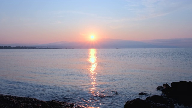 惊人美丽的日出在平静的海面上。黄色的太阳从海和山升起，太阳的路径在水上。阳光和太阳光反射在水面上。金色的光，橙色和金色的蓝天视频素材