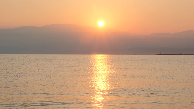 惊人美丽的日出在平静的海面上。黄色的太阳从海和山升起，太阳的路径在水上。阳光和太阳光反射在水面上。金色的光，橙色和金色的蓝天视频素材