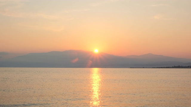 惊人美丽的日出在平静的海面上。黄色的太阳从海和山升起，太阳的路径在水上。阳光和太阳光反射在水面上。金色的光，橙色和金色的蓝天视频素材