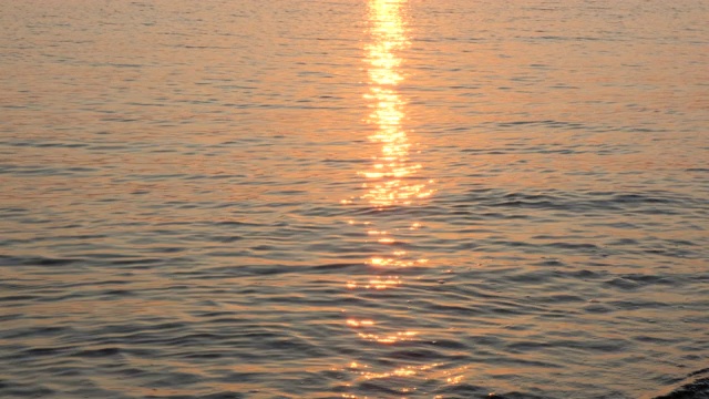 日出在平静的海面上，模糊地倒映着。黄色的太阳升起海面，太阳的路径在水上。海面上的阳光和太阳光反射在水面上。金色的灯光，橙色和蓝色的天空，大海的全景。放松视频素材