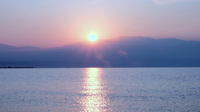 惊人美丽的日出在平静的海面上。黄色的太阳从海和山升起，太阳的路径在水上。阳光和太阳光反射在水面上。金色的光，橙色和金色的蓝天视频素材