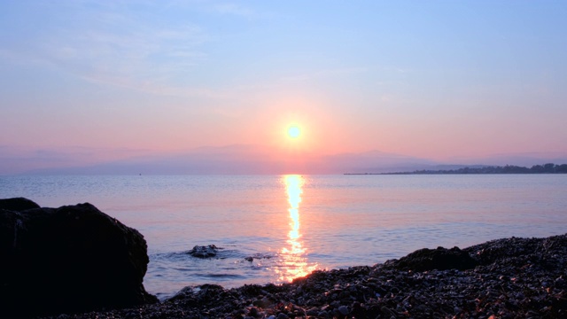 惊人美丽的日出在平静的海面上。黄色的太阳从海和山升起，太阳的路径在水上。阳光和太阳光反射在水面上。金色的光，橙色和金色的蓝天视频素材