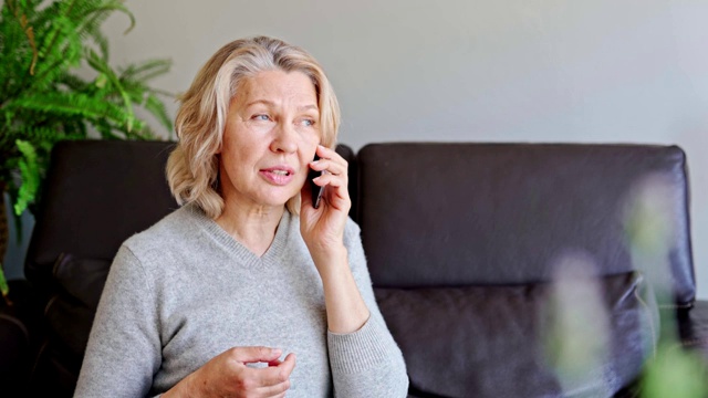 成熟的女人坐在家里的沙发上使用手机。视频素材