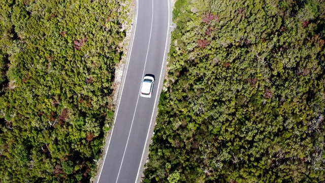 4K鸟瞰图白色家庭汽车行驶在绿色山丘的沥青道路上。视频素材