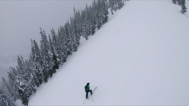 在冬季暴风雪中，男人爬着陡峭的雪坡视频素材