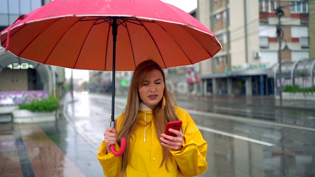 一个女人在雨天的雨伞下使用手机视频素材