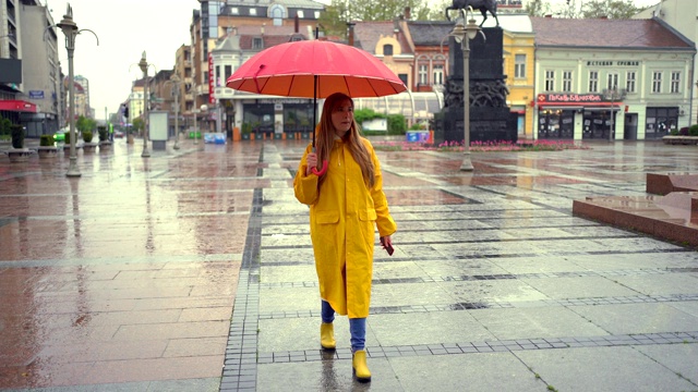 一个年轻女人在雨天走路，看着手机视频素材