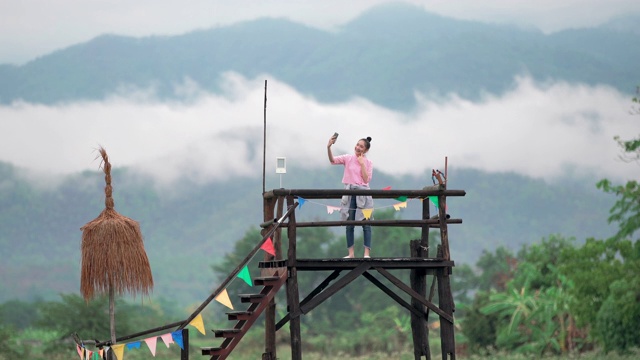 美丽的女孩用智能手机在清晨的雾和山的背景下自拍视频素材