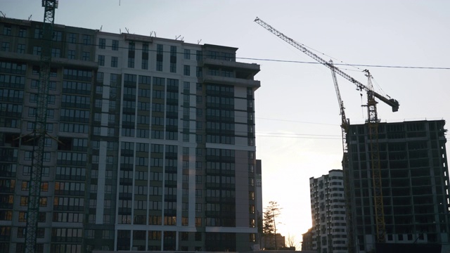 在美丽的日落建筑工地的时间流逝。太阳在地平线上落下，前面是未完工的建筑。时间流逝日落和剪影起重机在建筑工地视频素材