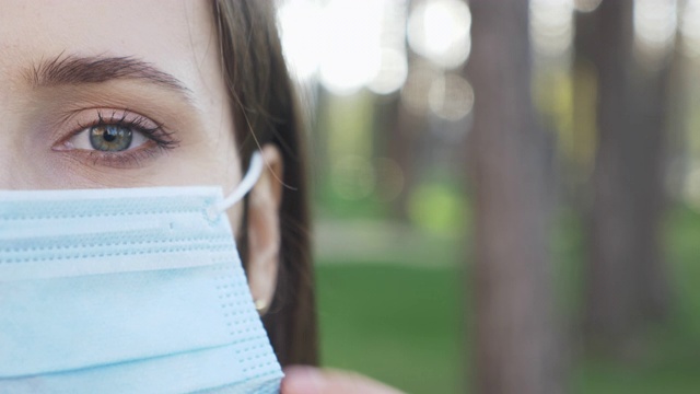 年轻美丽的女子在隔离期间摘下防护口罩的肖像。女孩戴医用蓝色口罩，预防和保护病毒感染。对流行病毒的恐慌，恐惧视频素材