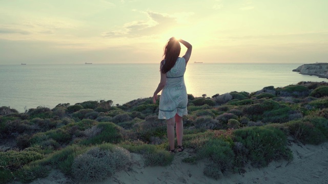 一个年轻女子站在海面上，看着夕阳。视频素材