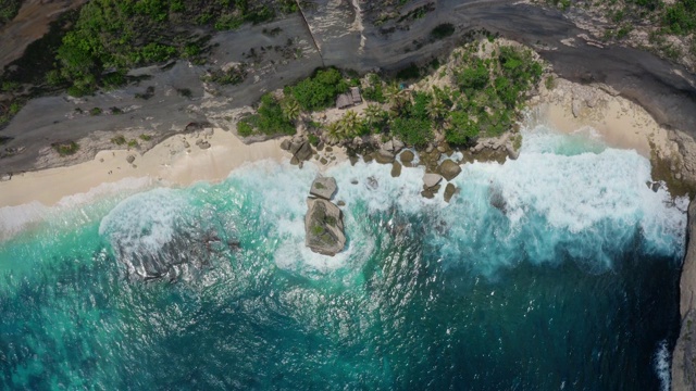 从上到下鸟瞰蔚蓝的海水，海浪冲击着野生的海滩视频素材