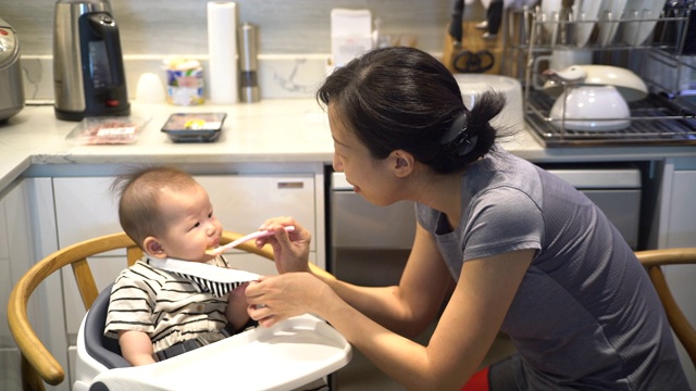 年轻的亚洲母亲在厨房用勺子给女婴喂食视频素材