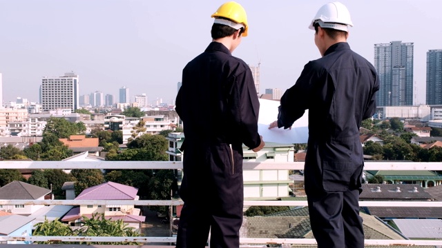 两位工程师站在建筑工地的屋顶上拿着图纸分析新楼的设计方案。视频素材