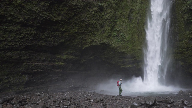 女子背包徒步旅行在一个绿色峡谷的瀑布视频素材