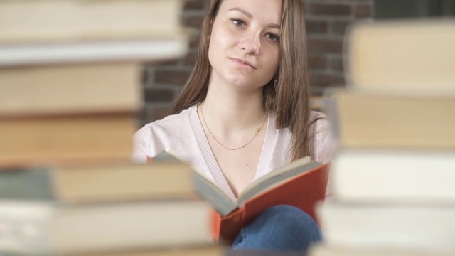 女学生坐在图书馆的一堆书中间。女人读的书。视频素材