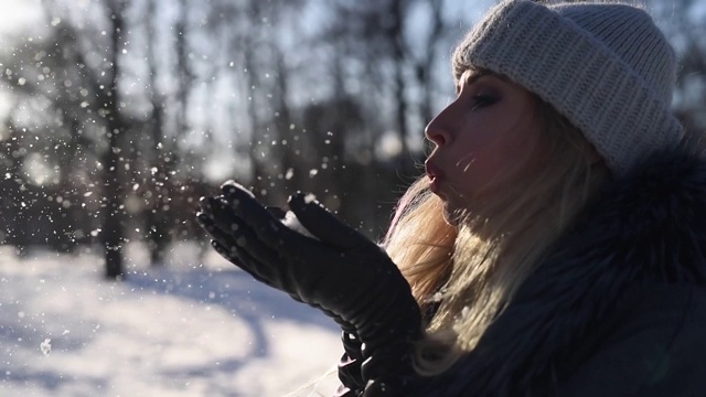 年轻女子在冬天的公园里吹雪，慢镜头。晴朗多雪的冬季天气视频素材