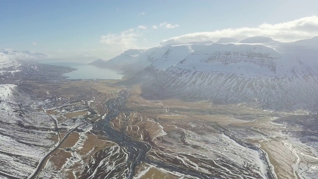 航拍，飞过冰雪覆盖的山脉，冰岛东部峡湾。冰岛乡村景观在春天或秋天的雪山季节之间。阳光明媚，适合旅游。视频素材